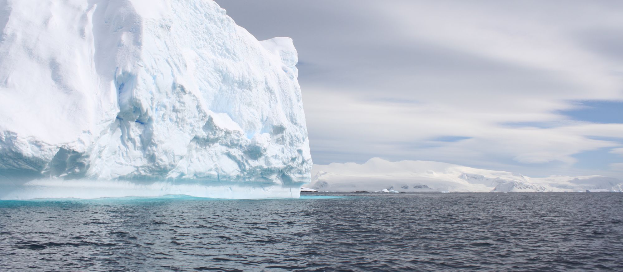 A tabular iceberg drifting under a pale sky, photographed from the water