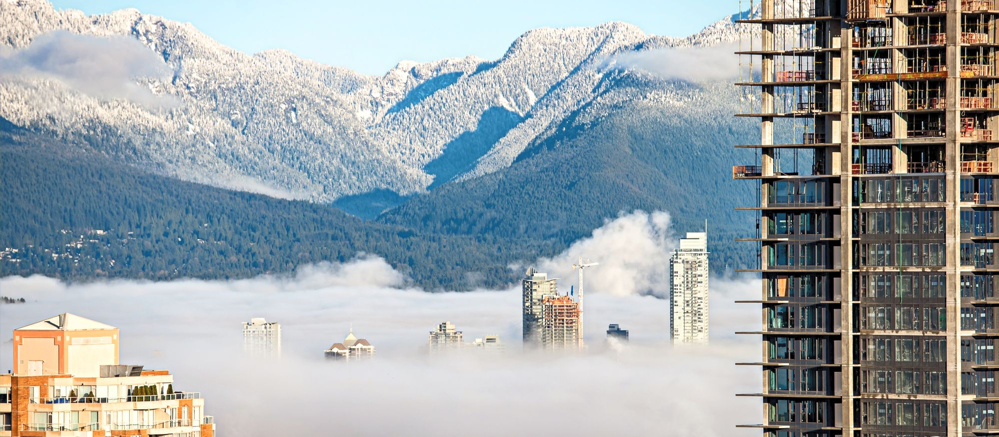 Tower blocks rising out of morning fog with snow-capped mountains behind